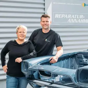 Zwei Mitarbeitende stehen vor einer Autowerkstatt bei der Reparaturannahme und Karosserie.