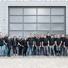 Ein Team von Kfz-Werkstatt-Mitarbeitern steht vor einer modernen Autowerkstatt.