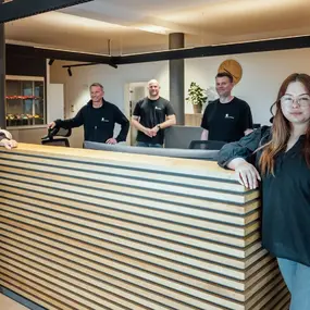 Fünf Personen stehen lächelnd hinter einem modernen Empfangstresen im Büro.
